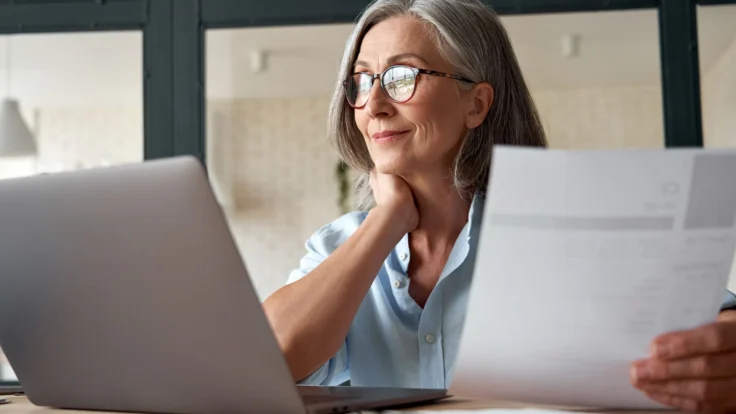 A woman is sitting at a desk with a laptop and papers in front of her.