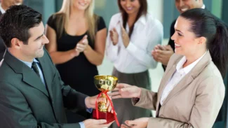 A woman is handing a trophy to a man in a business suit.