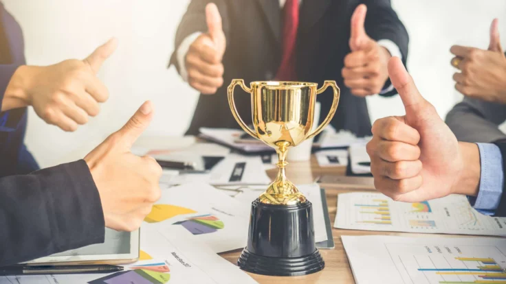 A group of business people holding a trophy and giving thumbs up.