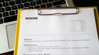 A clipboard with a resume on it next to a laptop.