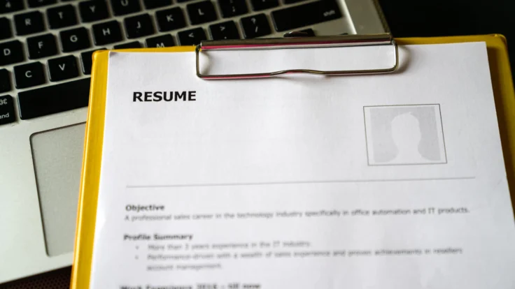 A clipboard with a resume on it next to a laptop.