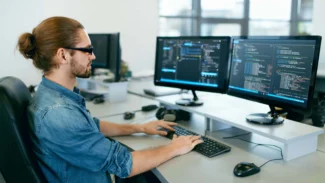 A man sitting at a desk with two monitors in front of him.