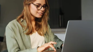 A woman wearing glasses is using a laptop.