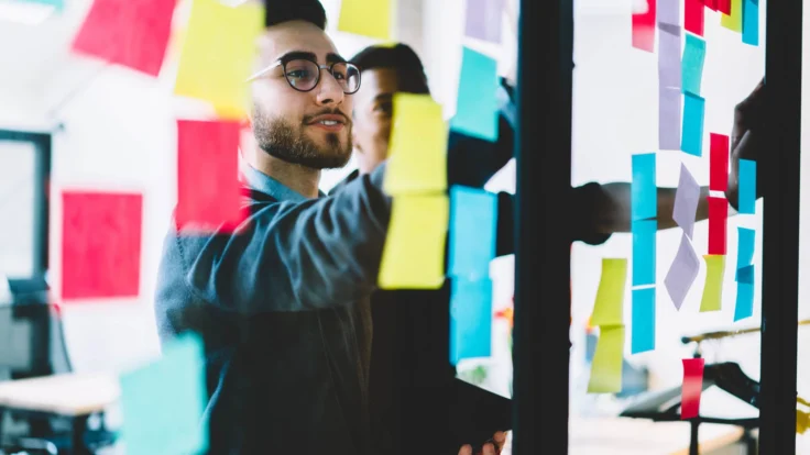 A group of people looking at sticky notes on a wall.