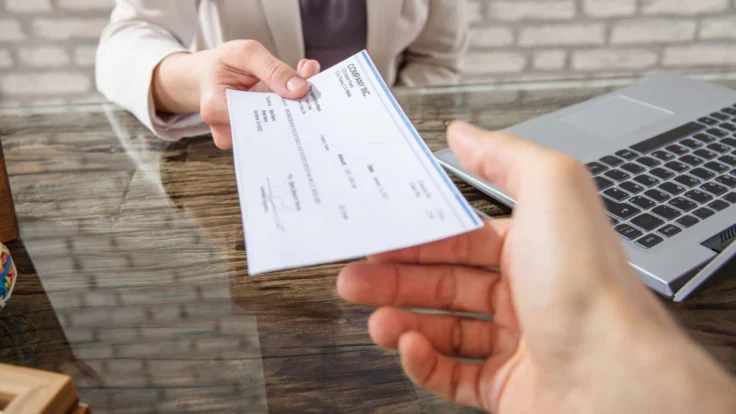 A person handing a check to another person at a desk.