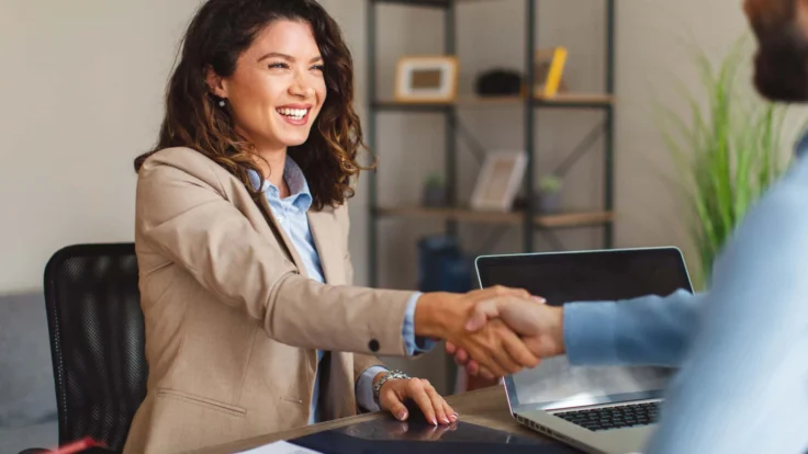 A woman shaking hands with a man at a desk.