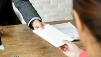 A businessman handing a letter to a woman at a desk.