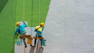 Two men painting a green wall.