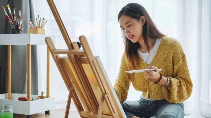 A woman is painting on an easel in her home.