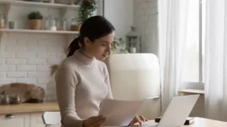 A woman sitting at a kitchen table with a laptop.