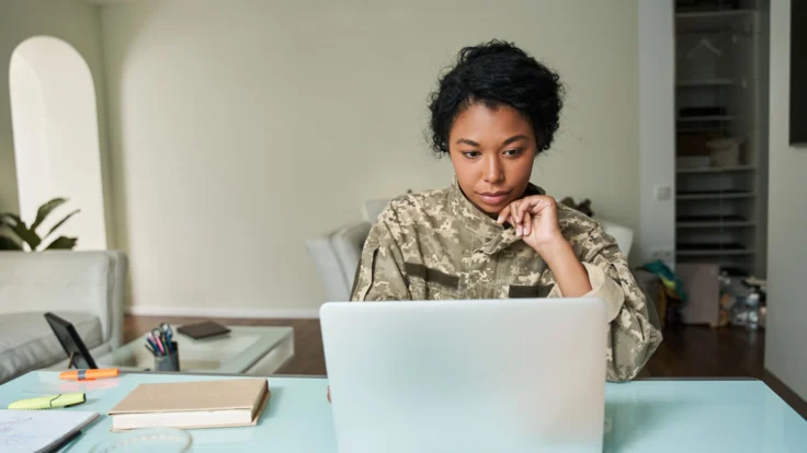 A woman in military uniform using a laptop at home.