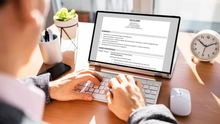 A man typing on a laptop with a resume on it.