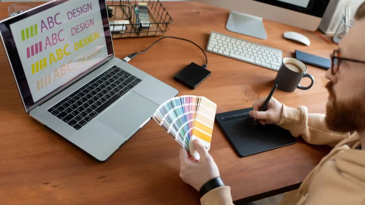 A man sitting at a desk with a laptop and color swatches.