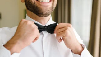 A man in a white shirt is putting on a bow tie.