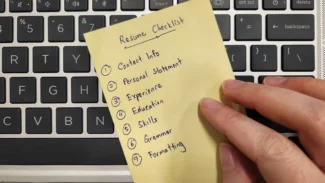 A person holding a yellow sticky note on a keyboard.