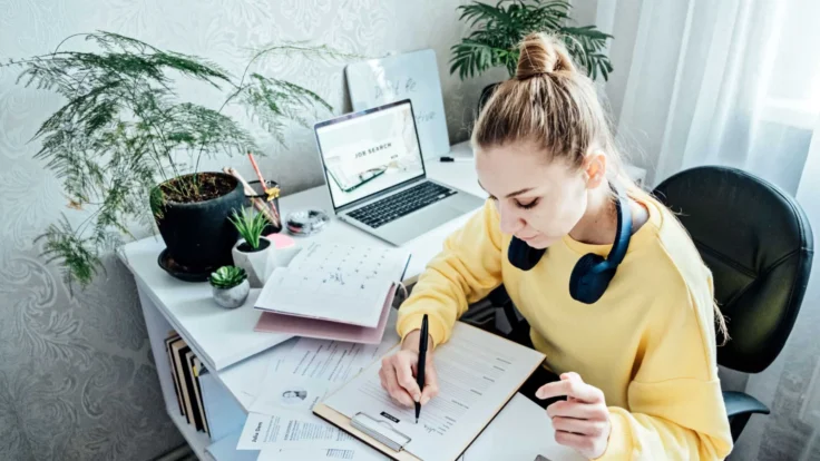 A woman is sitting at a desk and writing in a notebook.
