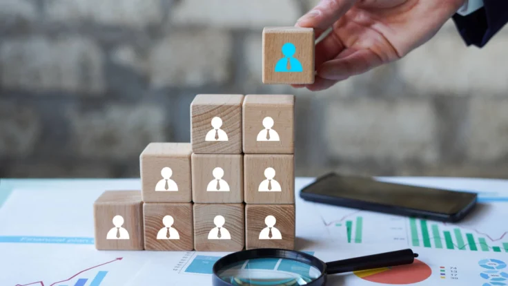 A businessman stacking wooden cubes with people icons on them.
