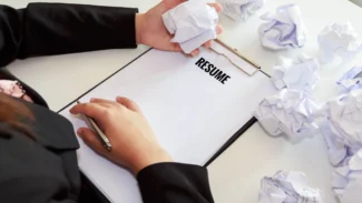 A woman writing a resume on a clipboard with crumpled paper.