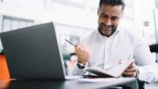 A man is sitting in front of a laptop and smiling.