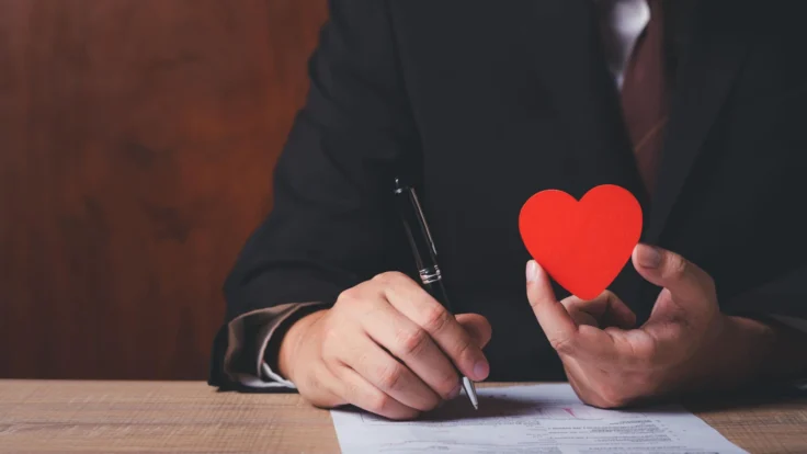 A man in a suit holding a red heart on a piece of paper.