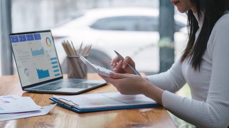 A woman sitting at a desk with a laptop and graphs on it.