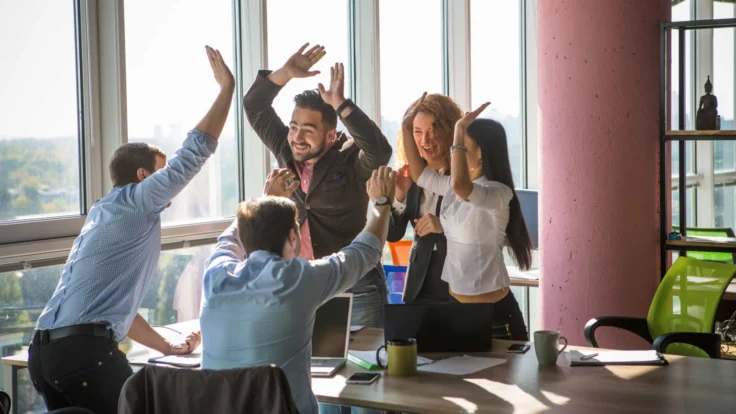 A group of business people raising their hands in an office.
