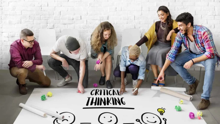 A group of people drawing the word critical thinking on a white board.