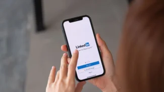 A woman holding a phone with linkedin on it.