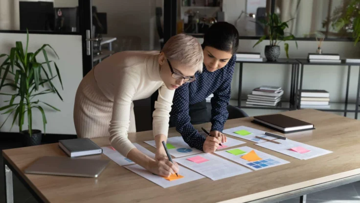 Two business women working at a table in an office.