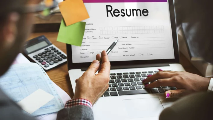 A person looking at a resume on a laptop.