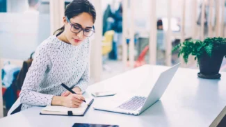 A woman writing on a laptop in an office.